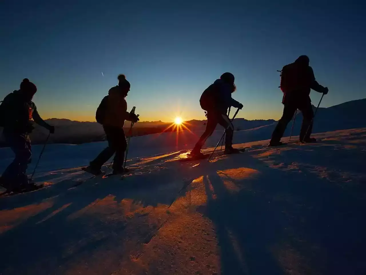 Eine Gruppe geht Schneeschuhwandern bei Sonneraufgang in den Bergen.